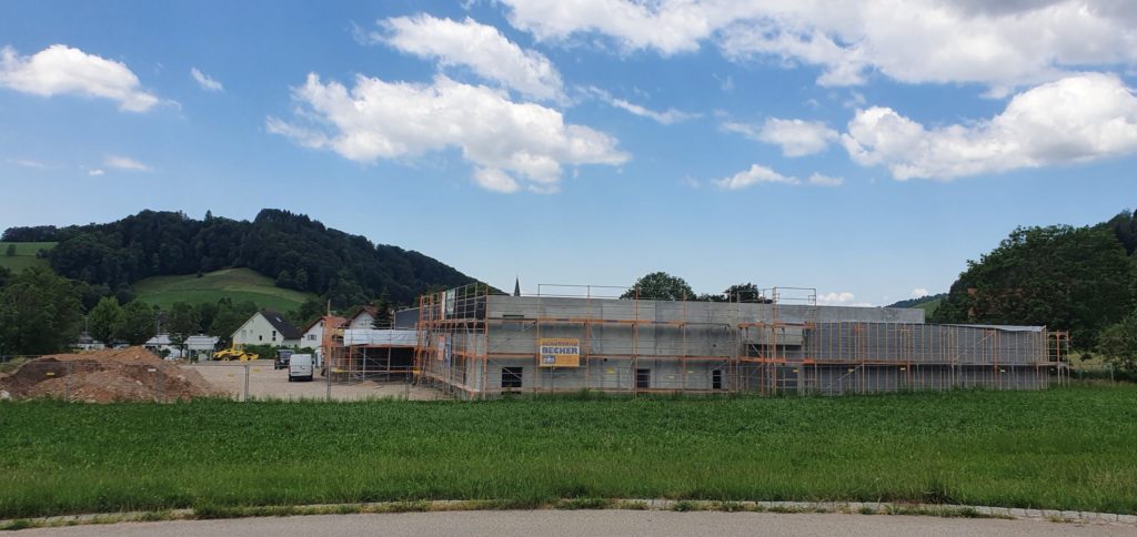 Bau eines neuen Gebäudes mit Gerüst in ländlicher Umgebung, umgeben von Wiesen und Hügeln.