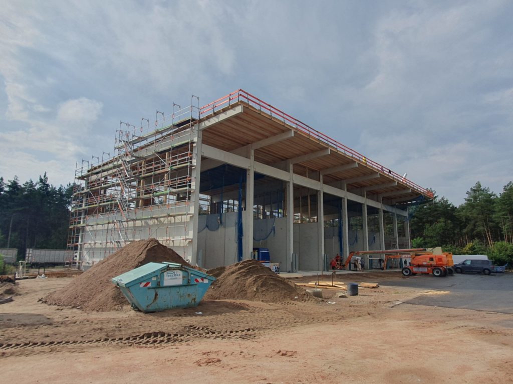 Ein im Bau befindliches Gebäude mit Gerüsten, Baumaschinen und Erdhaufen in einer bewaldeten Umgebung.