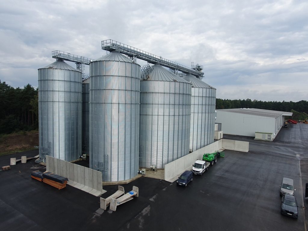 Moderne Silos zur Lagerung von Getreide neben einem Lagergebäude auf einem asphaltieren Gelände.