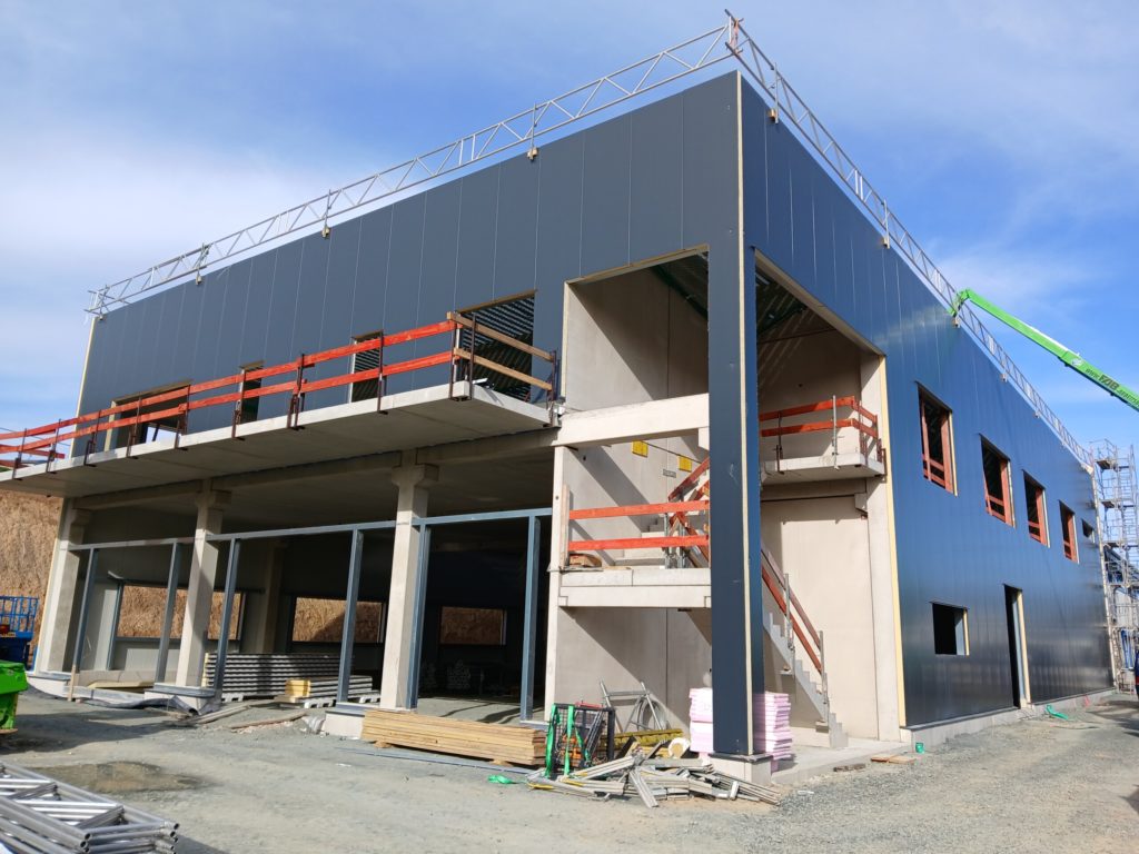 Neubau eines modernen Gebäudes mit Stahlverkleidung und Baustellenzubehör unter blauem Himmel.