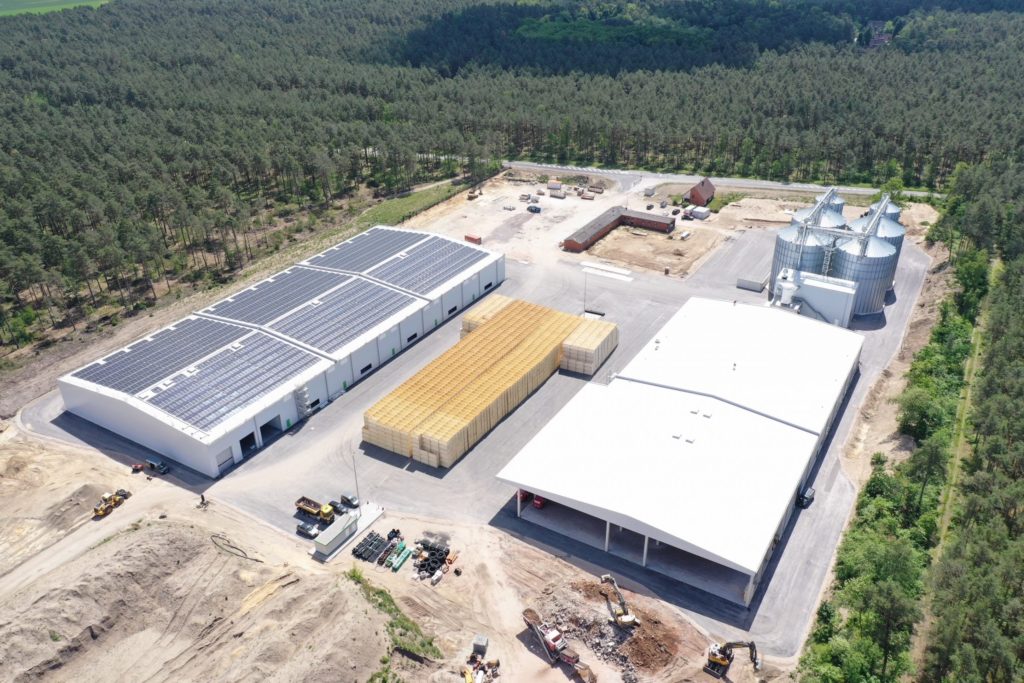 Luftaufnahme eines modernen Industriekomplexes mit Solarpanelen, Lagerhäusern und Silos in ländlicher Umgebung.
