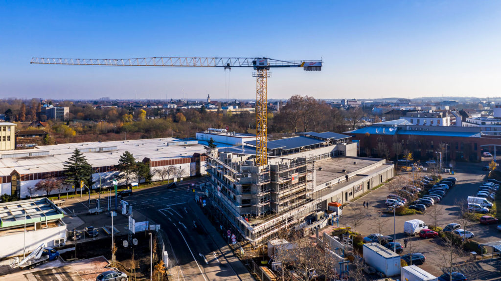 Bauprojekt mit Kran und neuem Gebäude in urbaner Umgebung, umgeben von Straßen und Bäumen.