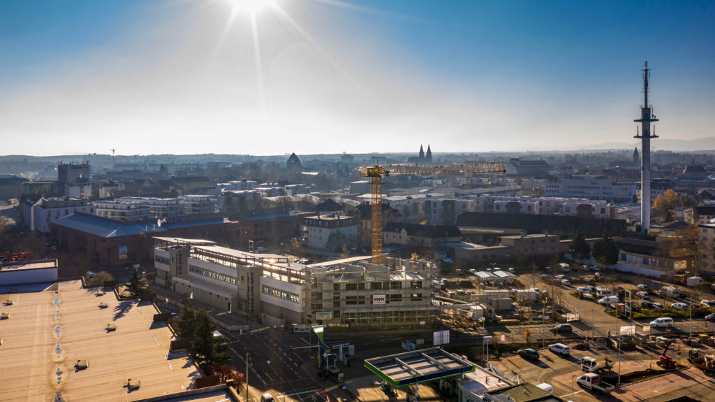 Blick auf eine Baustelle in der Stadt mit einem Kran, umgeben von modernen Gebäuden und einer klaren, sonnigen Atmosphäre.