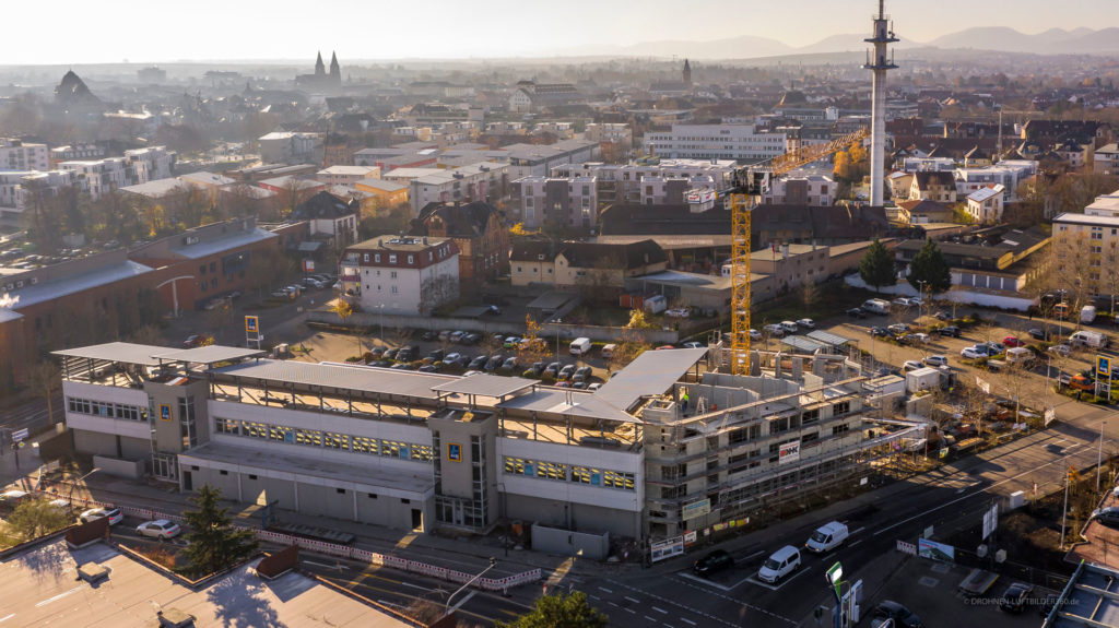 Blick auf die Baustelle eines neuen Gebäudes in einer Stadt mit Wohn- und Geschäftshäusern im Hintergrund.