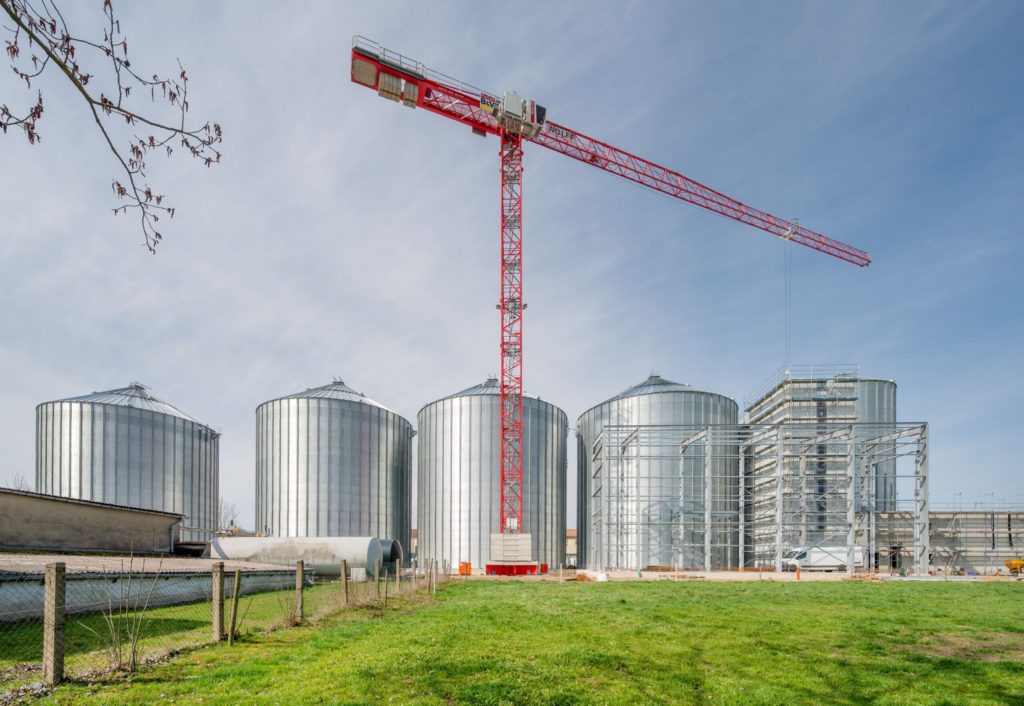 Silobauten mit einem Kran im Hintergrund, umgeben von Wiese und klarem Himmel, symbolisieren landwirtschaftlichen Fortschritt.