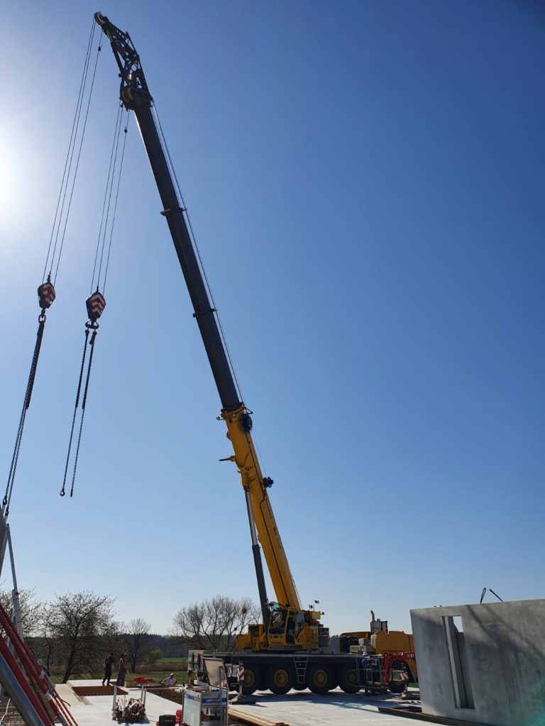 Ein gelber Kran hebt Lasten auf einer Baustelle unter klarem blauen Himmel.