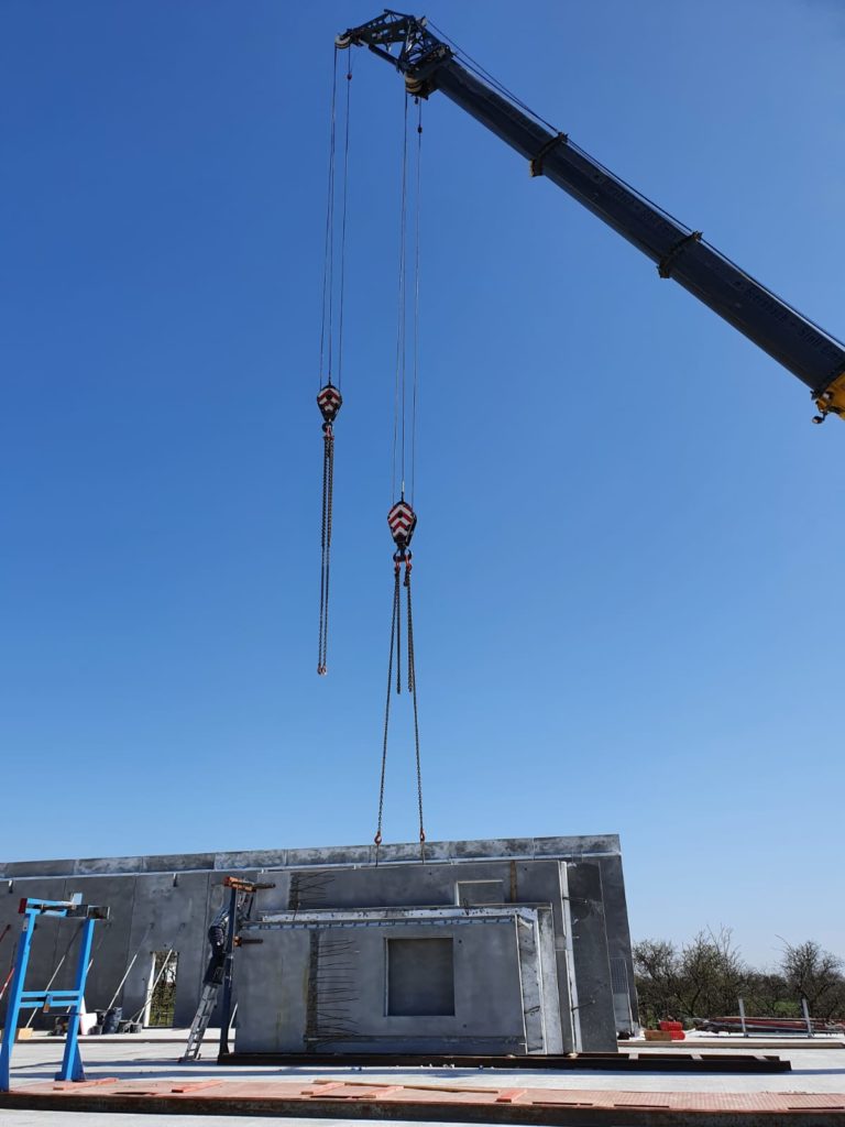 Baukran hebt Betonwände auf einer Baustelle unter klarem blauen Himmel.