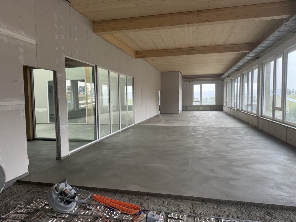 Heller, moderner Innenraum mit großen Fenstern und einem unvollendeten Boden, ideal für eine Neubauwohnung.