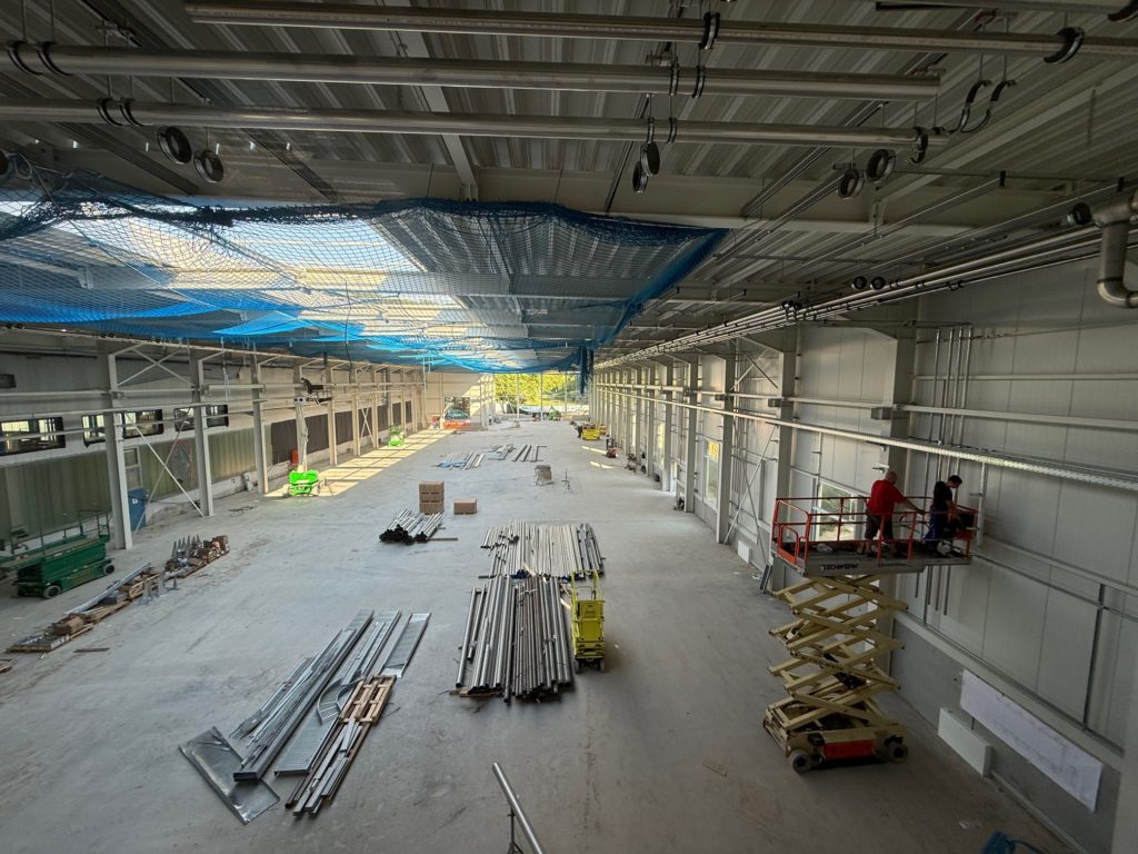 Bauarbeiten in einer großen Halle mit Baustellenmaterial und Arbeitern, die an der Decke arbeiten.