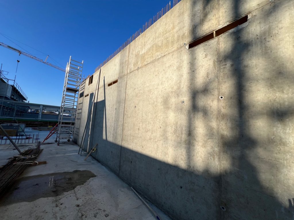 Bauarbeiter arbeiten an einer Betonwand mit Gerüst und blauem Himmel im Hintergrund.