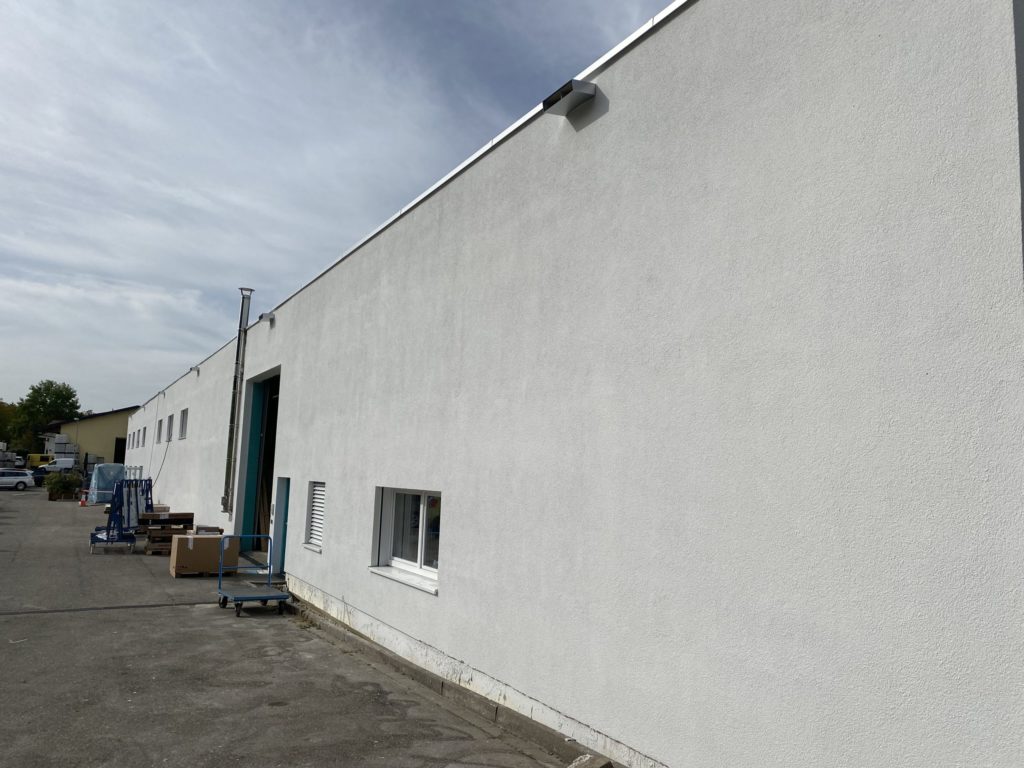 Weiße Lagerhalle mit offenen Türen, Fenster und einem Handwagen auf dem Hof.