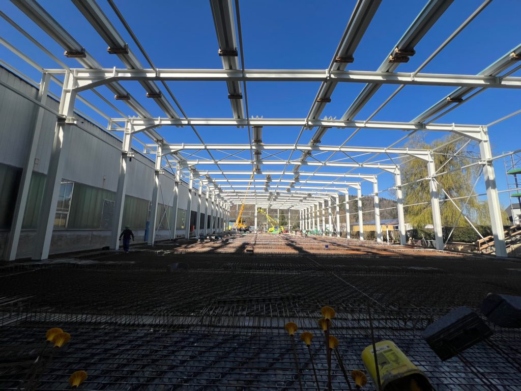 Blick auf eine große Baustelle mit Stahlrahmen und klarem Himmel, die auf den Bau eines neuen Gebäudes hinweist.