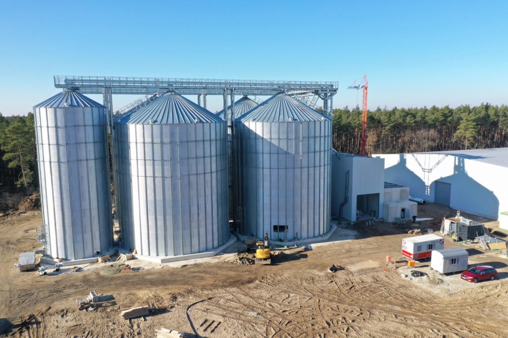 Drei große Silos stehen auf einem Baustellengelände unter klarem Himmel.