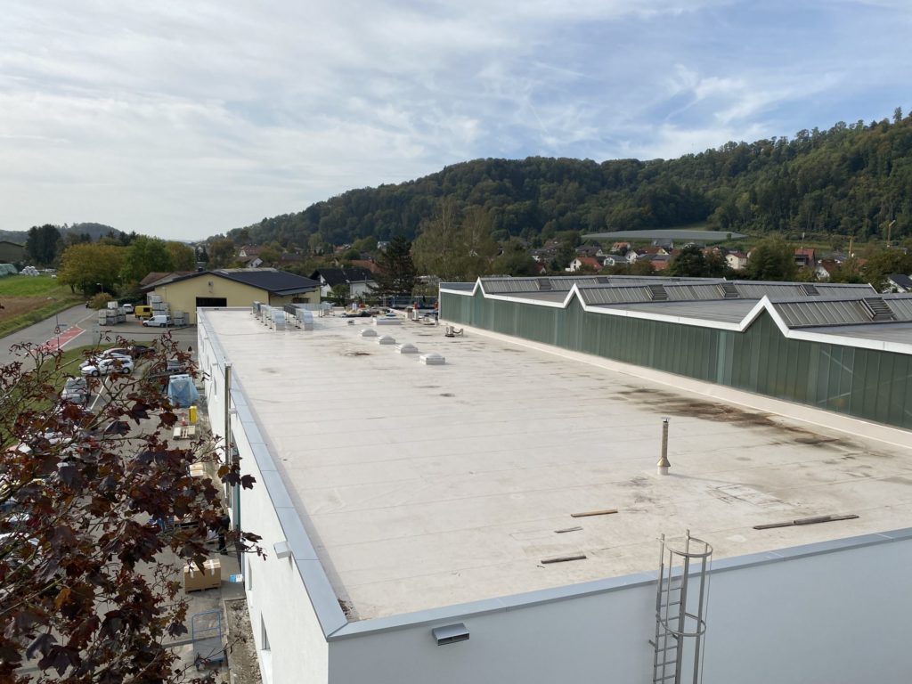 Dachansicht eines Gebäudes mit angrenzendem Parkplatz und umliegender Landschaft im Hintergrund.