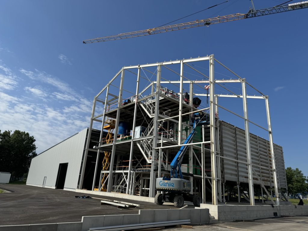 Bau eines Industriegebäudes mit Gerüst, Kran und Baustellenfahrzeug unter blauem Himmel.